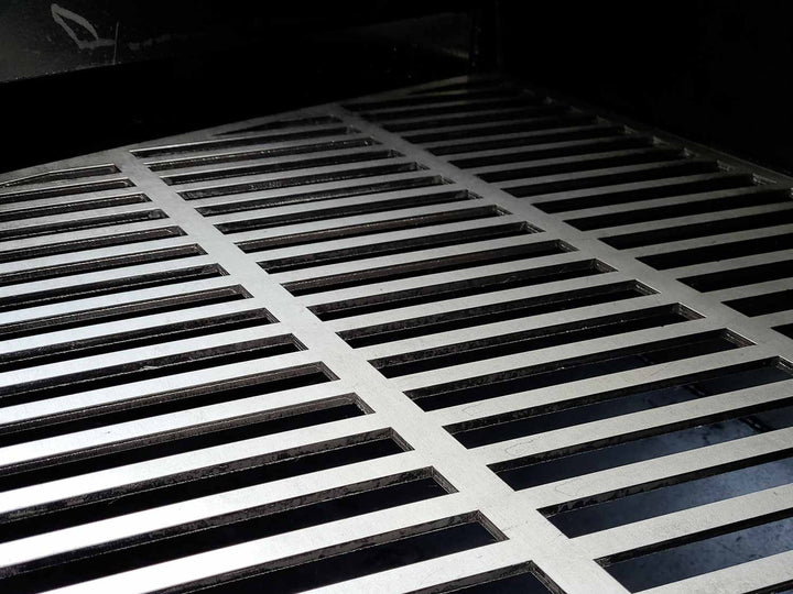Laser cut stainless steel cooking grates shown inside of an offset smoker