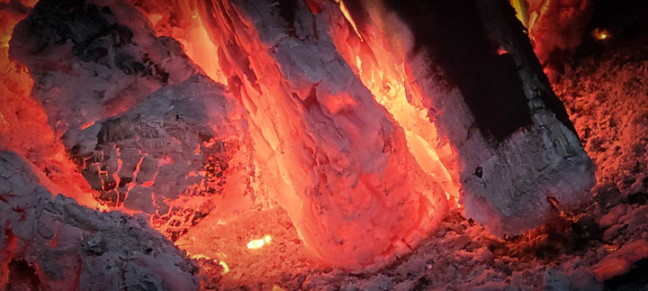 Several logs burnt down to a very hot, glowing red coal bed within the firebox of an offset smoker